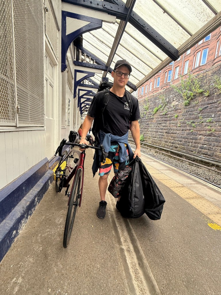 Loren with his loaded bike and bags on a train platform in Scotland